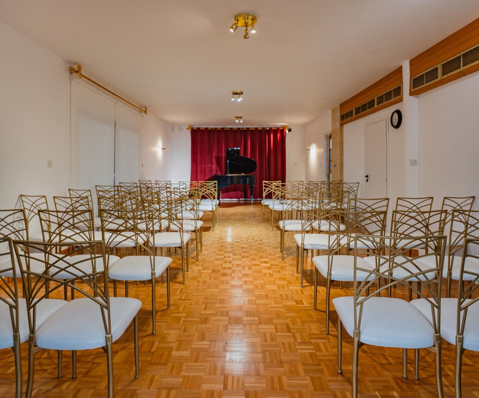 The recital hall: rows of gold chairs facing a grand piano beneath a red velvet curtain